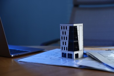 Photo of Real estate. Apartment building model, architectural drawings and laptop on table indoors, closeup