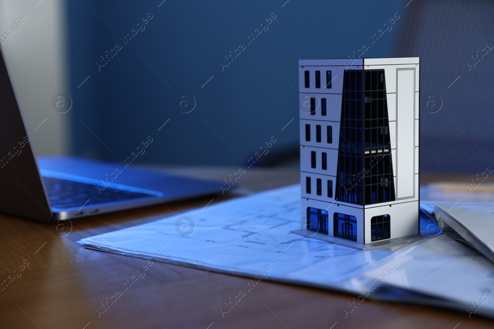 Photo of Real estate. Apartment building model, architectural drawings and laptop on table indoors, closeup