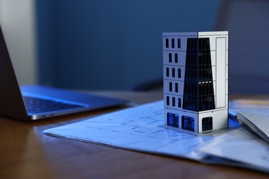 Photo of Real estate. Apartment building model, architectural drawings and laptop on table indoors, closeup