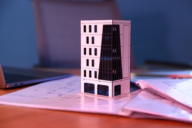Photo of Real estate. Apartment building model, architectural drawings and laptop on table in neon lights, closeup