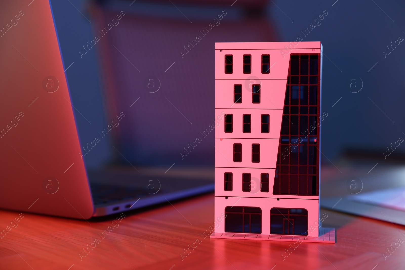 Photo of Real estate. Apartment building model and laptop on table in neon lights , closeup