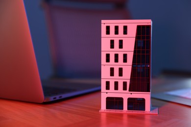 Photo of Real estate. Apartment building model and laptop on table in neon lights , closeup