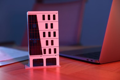 Photo of Real estate. Apartment building model and laptop on table in neon lights , closeup