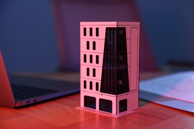 Photo of Real estate. Apartment building model and laptop on table in neon lights , closeup