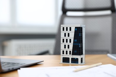 Photo of Real estate. Apartment building model, paperwork and laptop on table indoors, closeup. Space for text