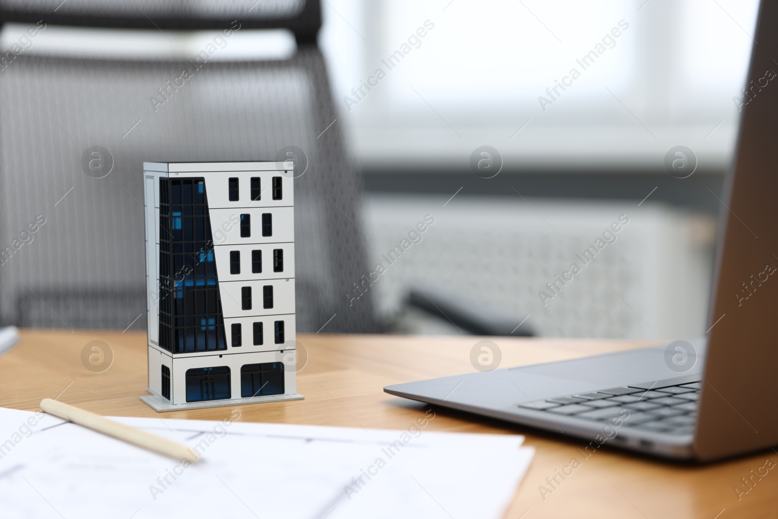 Photo of Real estate. Apartment building model, paperwork and laptop on table indoors, closeup