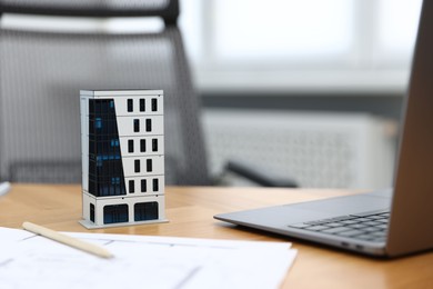Photo of Real estate. Apartment building model, paperwork and laptop on table indoors, closeup