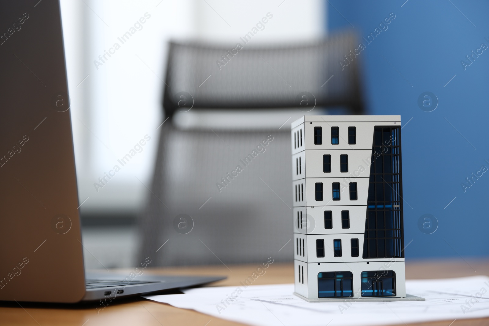 Photo of Real estate. Apartment building model, paperwork and laptop on table indoors, closeup
