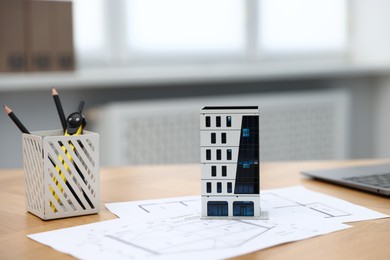 Photo of Real estate. Apartment building model and paperwork on table indoors, closeup