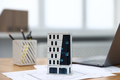 Photo of Real estate. Apartment building model, architectural drawings and laptop on table indoors, closeup