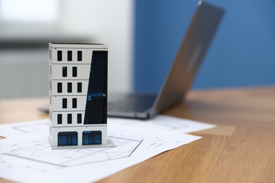 Photo of Real estate. Apartment building model, architectural drawings and laptop on table indoors, closeup