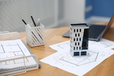 Photo of Real estate. Apartment building model, architectural drawings and laptop on table indoors, closeup