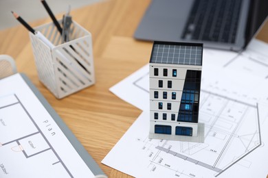 Photo of Real estate. Apartment building model, architectural drawings and laptop on table, closeup