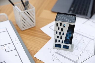 Photo of Real estate. Apartment building model, architectural drawings and laptop on table, closeup