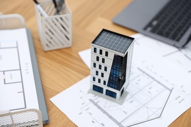 Photo of Real estate. Apartment building model, architectural drawings and laptop on table, closeup