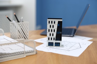 Photo of Real estate. Apartment building model, architectural drawings and laptop on table indoors, closeup