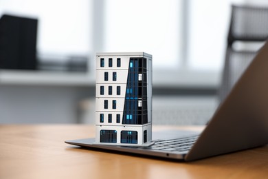 Photo of Real estate. Apartment building model and laptop on table indoors, closeup
