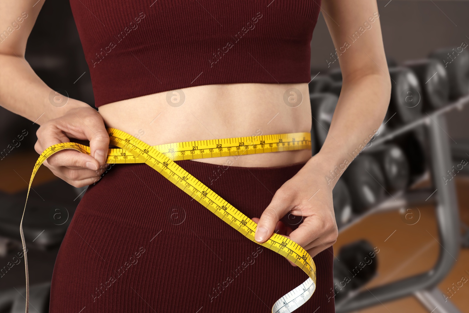 Athletic woman with flat belly and measuring tape in gym, closeup Image of Athletic woman with flat belly and measuring tape in gym, closeup
