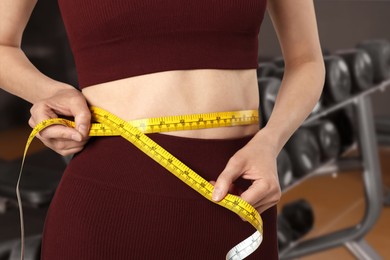Image of Athletic woman with flat belly and measuring tape in gym, closeup