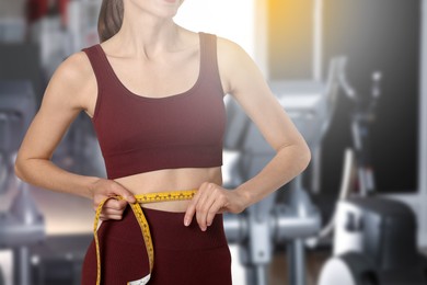 Image of Athletic woman with flat belly and measuring tape in gym, closeup