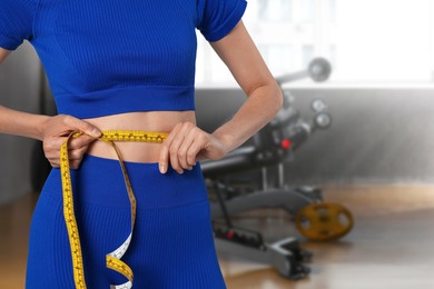 Image of Athletic woman with flat belly and measuring tape in gym, closeup