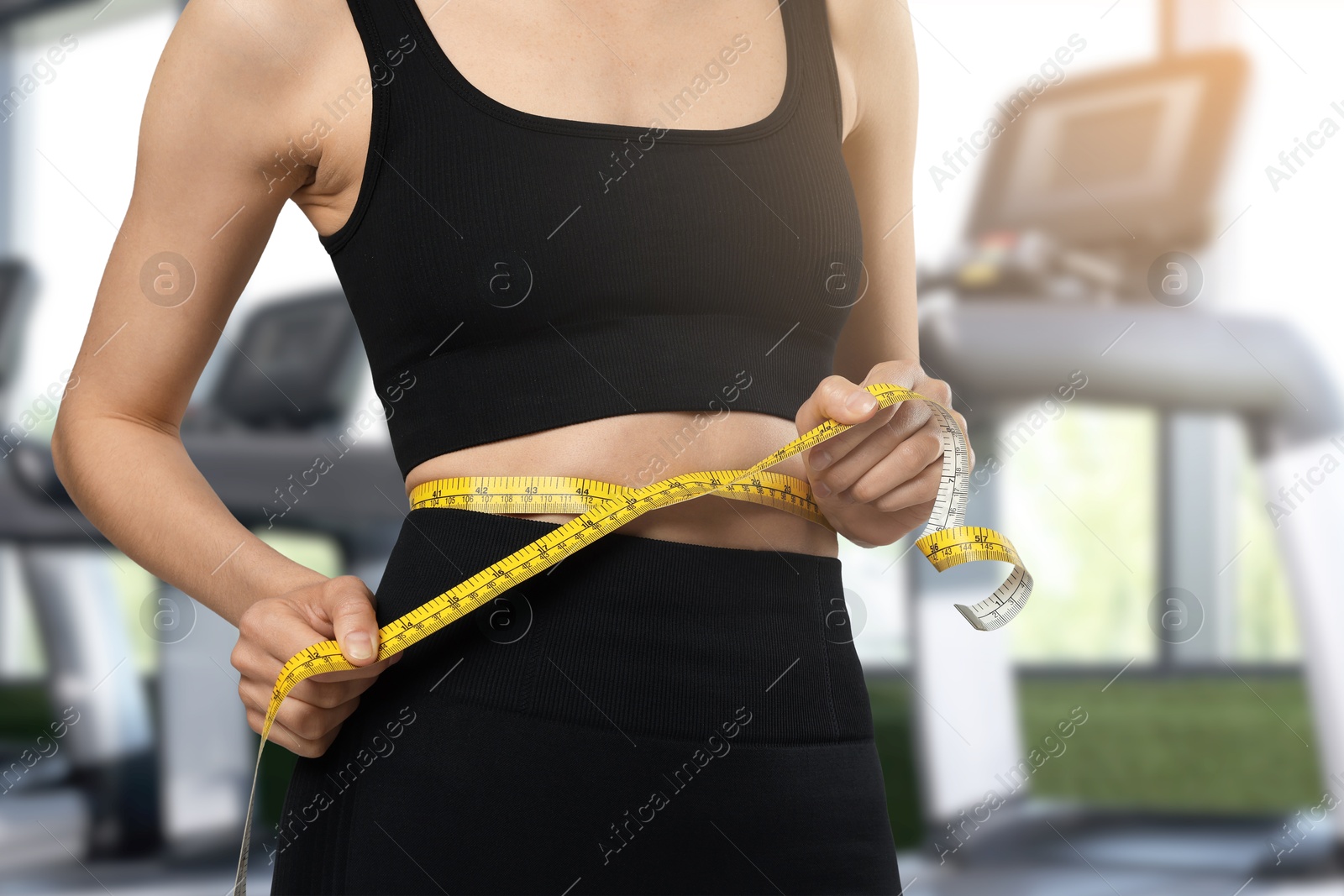 Image of Athletic woman with flat belly and measuring tape in gym, closeup