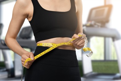 Image of Athletic woman with flat belly and measuring tape in gym, closeup