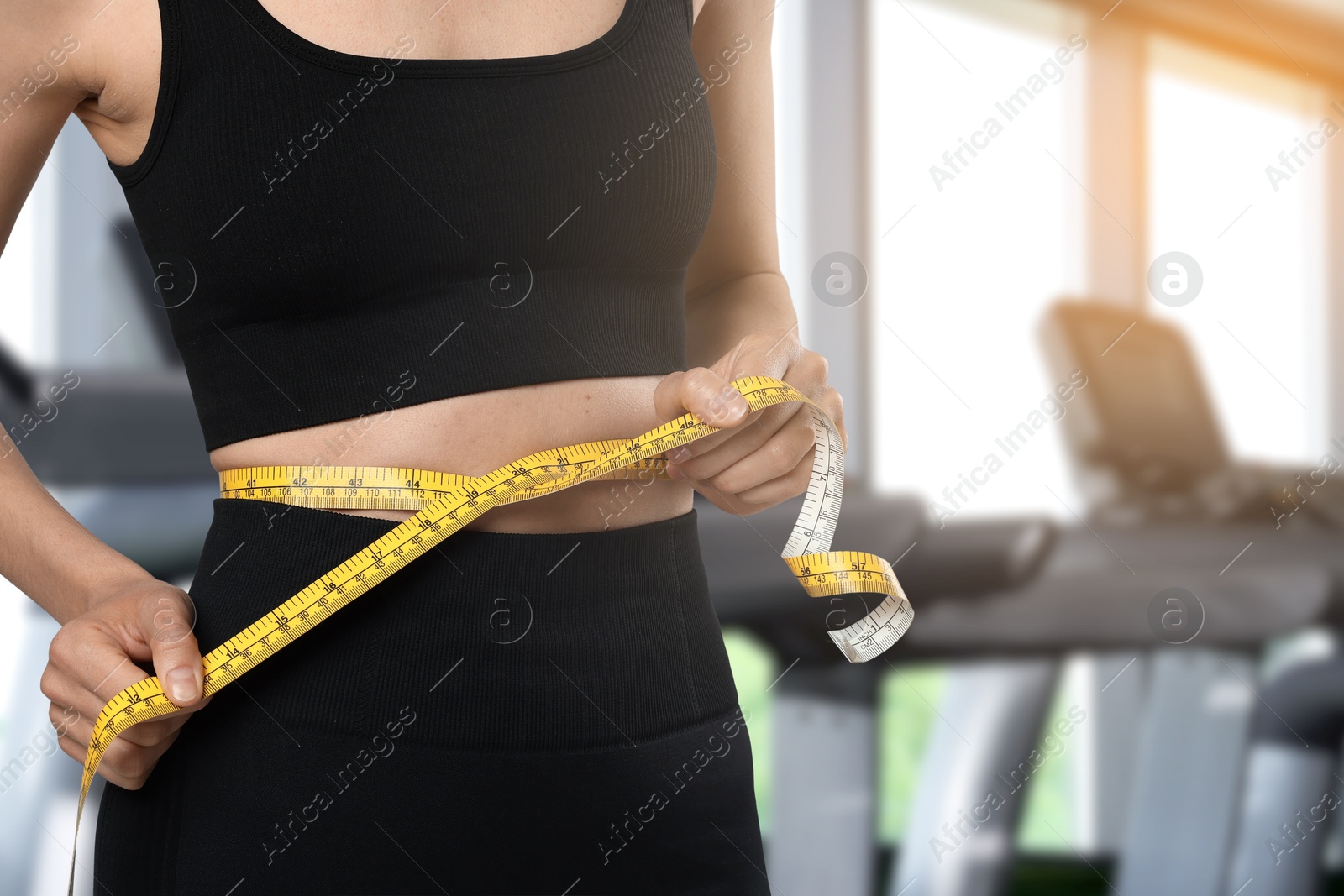 Image of Athletic woman with flat belly and measuring tape in gym, closeup