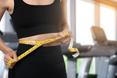 Image of Athletic woman with flat belly and measuring tape in gym, closeup