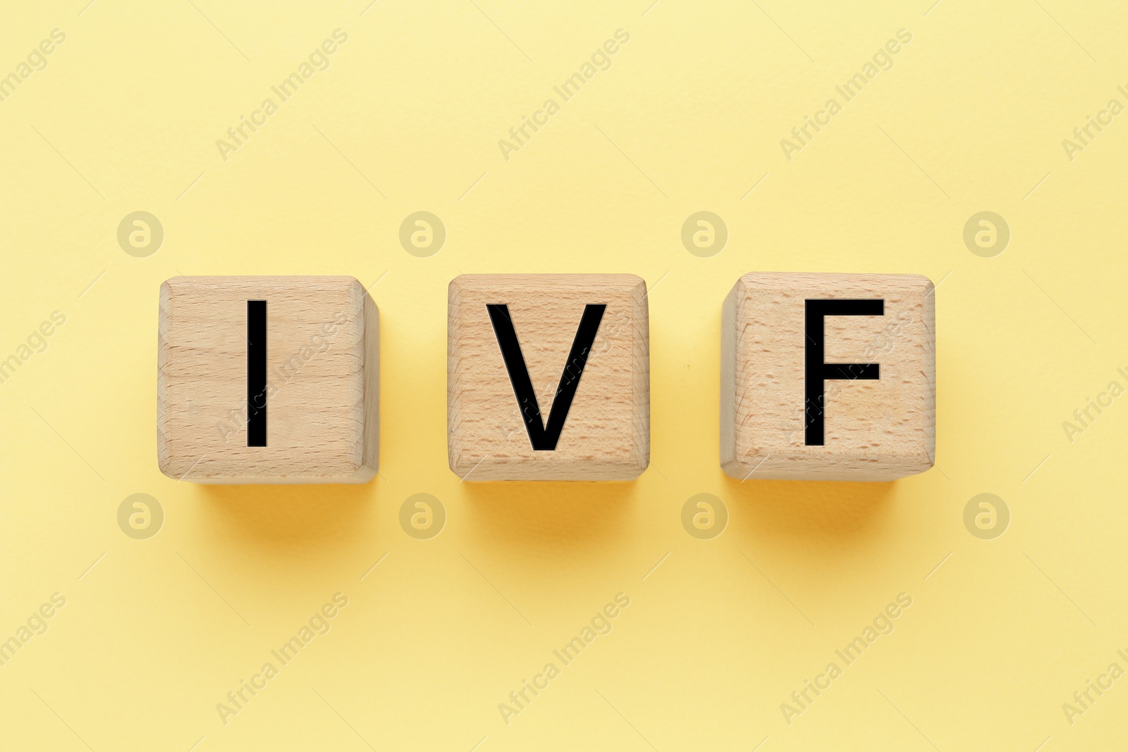 Image of In vitro fertilization. Wooden cubes with abbreviation IVF on pale yellow background, top view