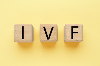 Image of In vitro fertilization. Wooden cubes with abbreviation IVF on pale yellow background, top view