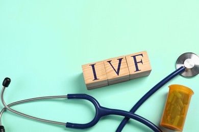 Image of In vitro fertilization. Wooden cubes with abbreviation IVF, pills and stethoscope on turquoise background, top view