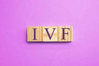 Image of In vitro fertilization. Wooden cubes with abbreviation IVF on violet background, top view