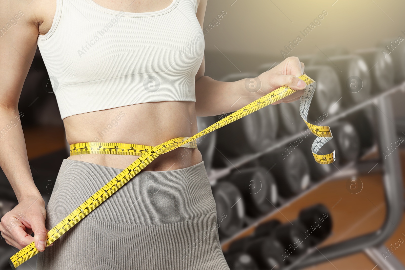 Image of Athletic woman with flat belly and measuring tape in gym, closeup