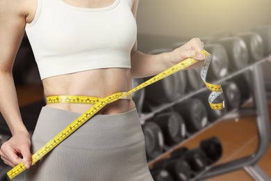 Image of Athletic woman with flat belly and measuring tape in gym, closeup