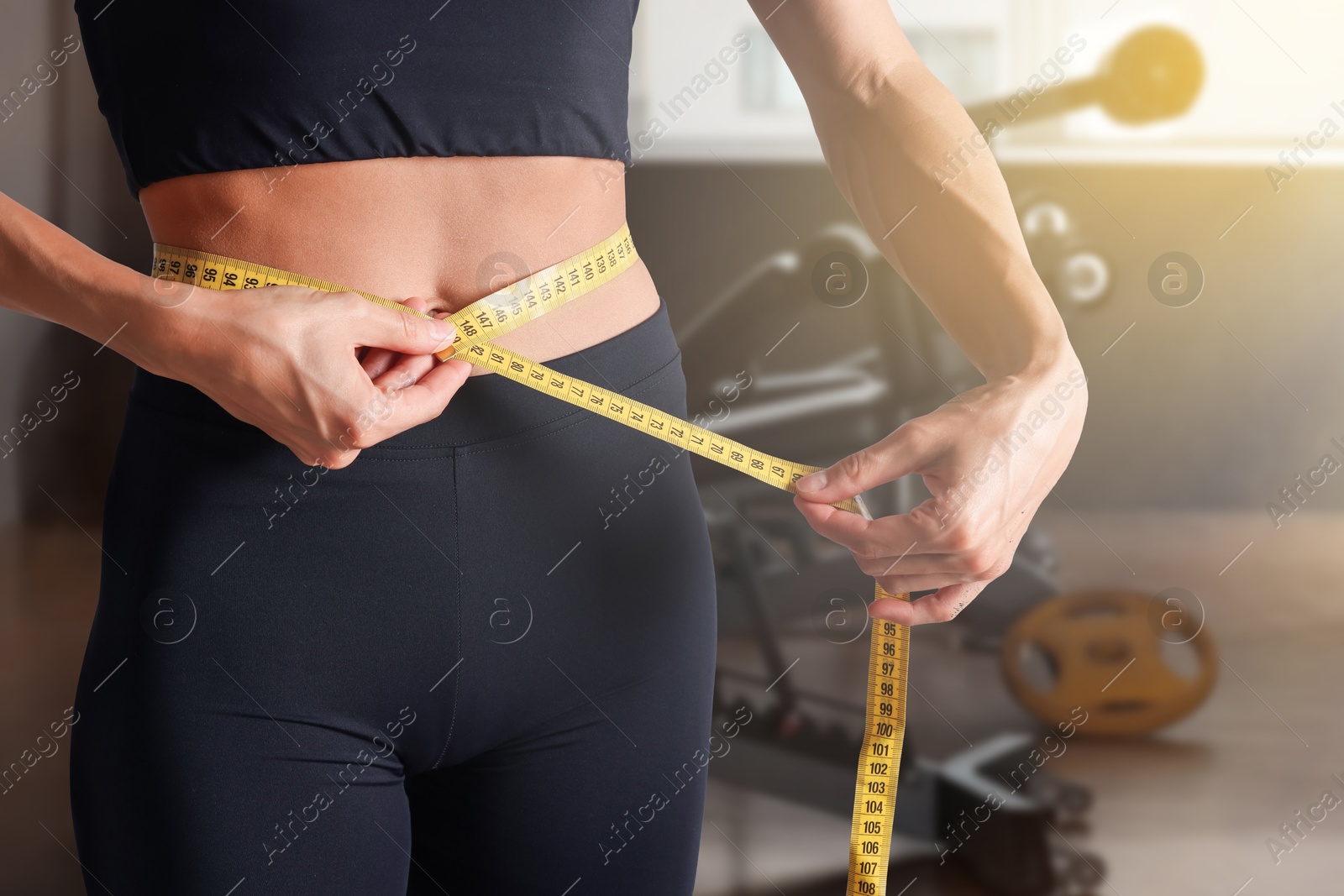 Image of Athletic woman with flat belly and measuring tape in gym, closeup