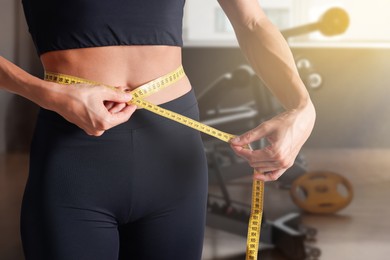Image of Athletic woman with flat belly and measuring tape in gym, closeup