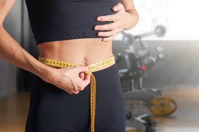 Image of Athletic woman with flat belly and measuring tape in gym, closeup