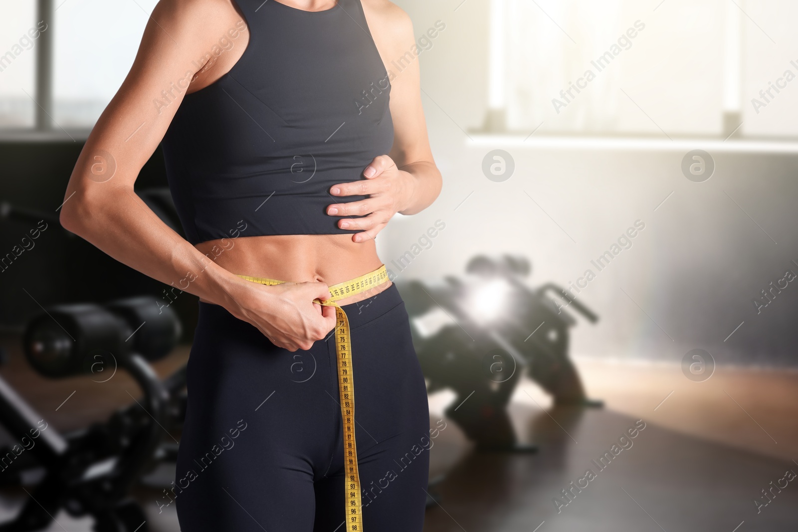 Image of Athletic woman with flat belly and measuring tape in gym, closeup