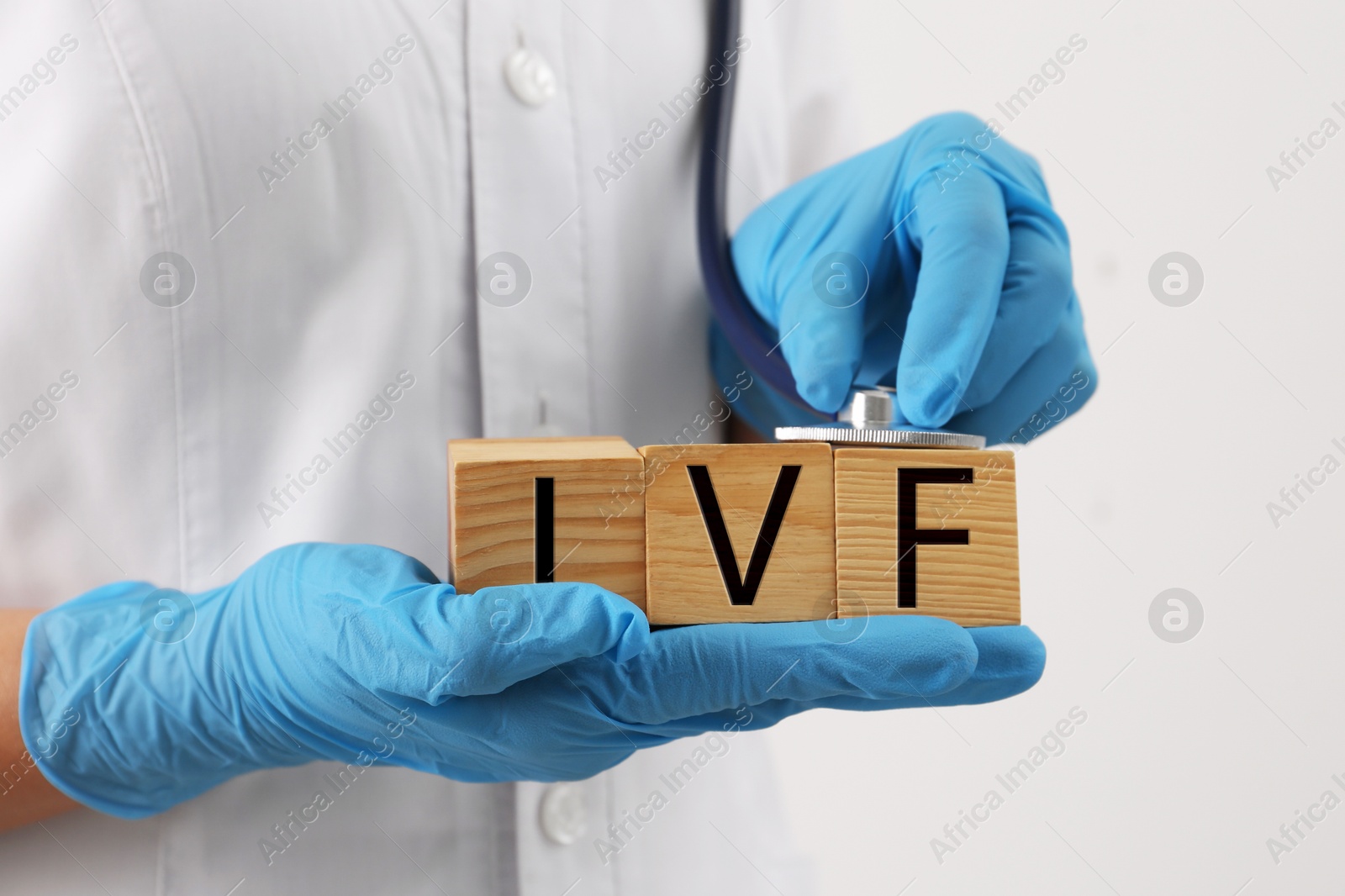Image of In vitro fertilization. Doctor holding wooden cubes with abbreviation IVF against white background, closeup
