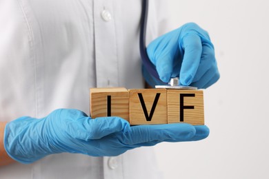 Image of In vitro fertilization. Doctor holding wooden cubes with abbreviation IVF against white background, closeup