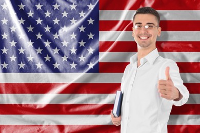 Image of Student or teacher with book showing thumbs-up against flag of USA. Language school