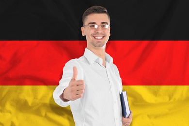 Image of Student or teacher with book showing thumbs-up against flag of Germany. Language school