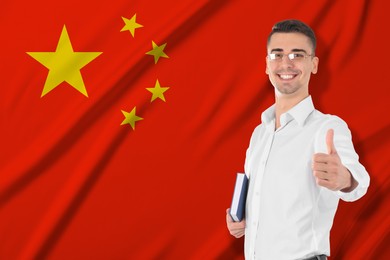 Image of Student or teacher with book showing thumbs-up against flag of China. Language school