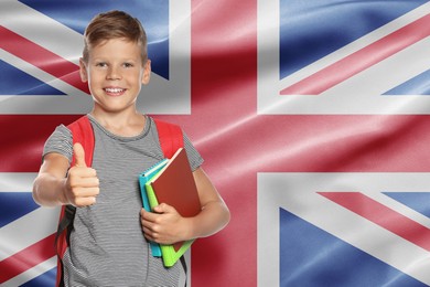 Image of Little boy with backpack and stationery showing thumbs-up against flag of United Kingdom. Language school