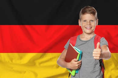 Image of Little boy with backpack and stationery showing thumbs-up against flag of Germany. Language school