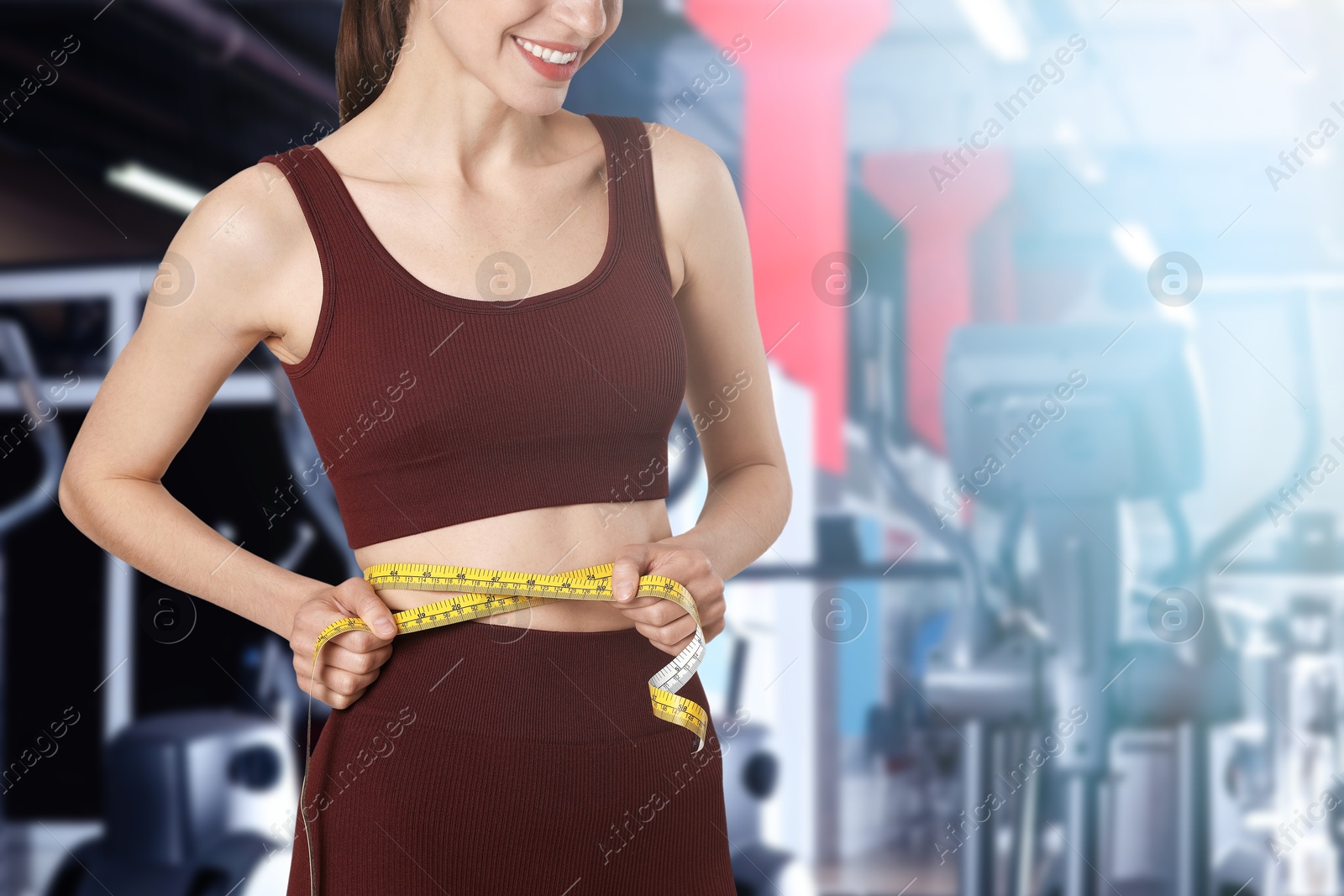 Athletic woman with flat belly and measuring tape in gym, closeup Image of Athletic woman with flat belly and measuring tape in gym, closeup