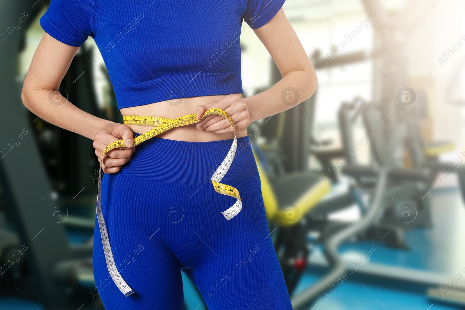 Athletic woman with flat belly and measuring tape in gym, closeup Image of Athletic woman with flat belly and measuring tape in gym, closeup