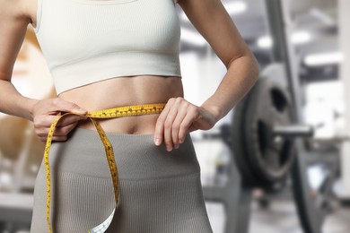 Image of Athletic woman with flat belly and measuring tape in gym, closeup