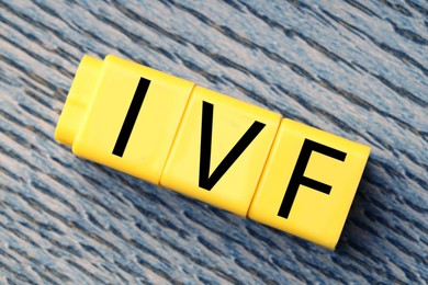 Image of In vitro fertilization. Yellow cubes with abbreviation IVF on wooden background, top view